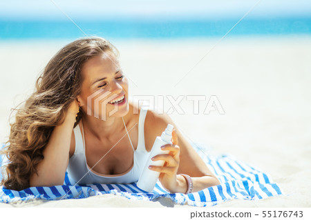 woman with SPF laying on striped towel on ocean shore 55176743