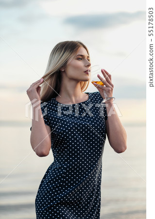 A young attractive blond woman, in a blue dress, walks along the seashore. Portrait of a smiling 55178503