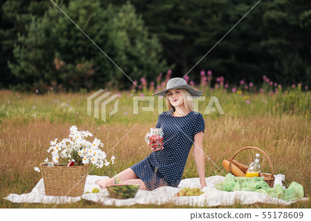 Young attractive woman in a blue dress at an outdoor picnic. A basket with daisies, watermelon Young attractive woman in a blue dress at an outdoor picnic. A basket with daisies, watermelon 55178609