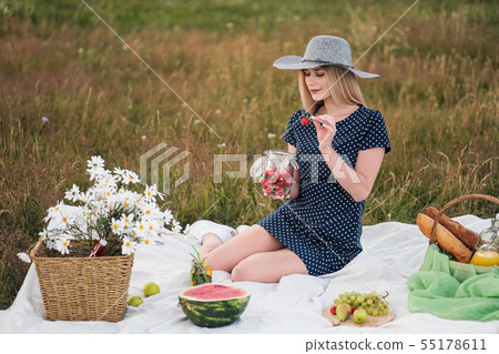 Young attractive woman in a blue dress at an outdoor picnic. A basket with daisies, watermelon Young attractive woman in a blue dress at an outdoor picnic. A basket with daisies, watermelon 55178611