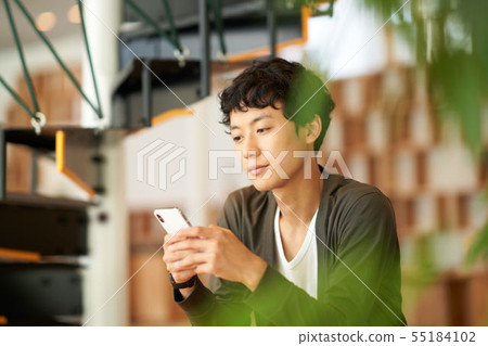 A man in his twenties who is operating a smartphone A man in his twenties who is operating a smartphone 55184102