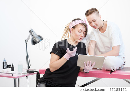 Professional tattoo master woman shows sketches on the tablet to the client girl. Discussion future 55185151