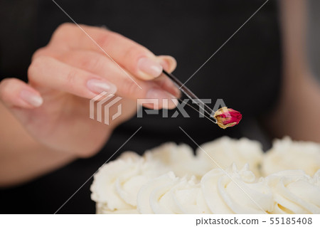 An attractive young female brunette confectioner decorates a white cake with small red flowers of An attractive young female brunette confectioner decorates a white cake with small red flowers of 55185408