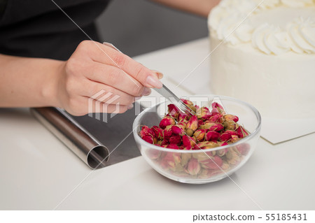 An attractive young female brunette confectioner decorates a white cake with small red flowers of An attractive young female brunette confectioner decorates a white cake with small red flowers of 55185431