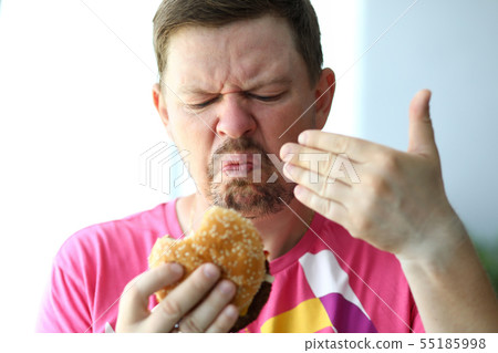 Unhappy man sniffing suspicious burger examining its freshness 55185998