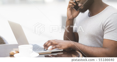 African american man typing on laptop and talking on cellphone 55186640