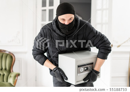 Thief looking at the camera with black balaclava stealing modern Electronic safe box. The burglar 55188733