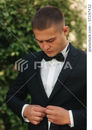 Young man walking in the park. Handsome groom in black suit Young man walking in the park. Handsome groom in black suit 55197432