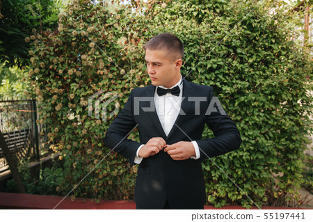 Young man walking in the park. Handsome groom in black suit Young man walking in the park. Handsome groom in black suit 55197441