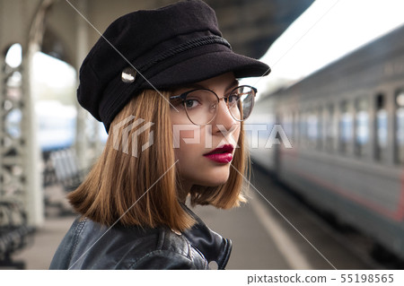 Attractive young woman millenial in black clothes and a hat and glasses at the railway station next 55198565