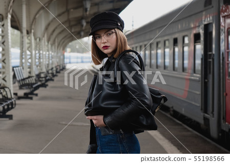 Attractive young woman millenial in black clothes and a hat and glasses at the railway station next Attractive young woman millenial in black clothes and a hat and glasses at the railway station next 55198566