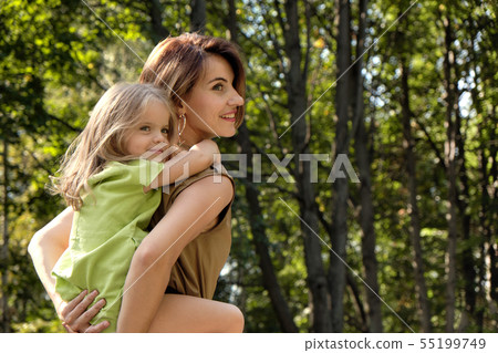 Family happiness. Cute young daughter riding her mom's back, on the nature in the park. Concept mom 55199749
