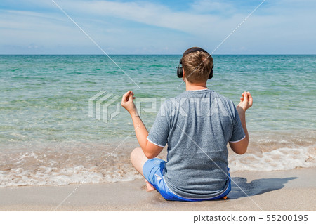 Happy young man sitting on the beach listening to 55200195