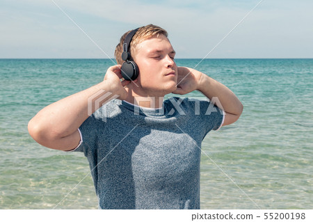 Portrait of a young man on the beach listening to 55200198