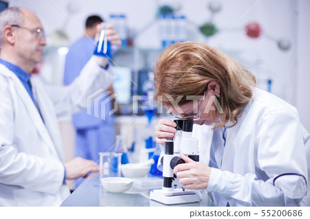 Middle age female chemist engineer working on a microscope in a laboratory 55200686