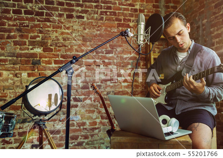 Young man recording music, playing guitar and singing at home Young man recording music, playing guitar and singing at home 55201766