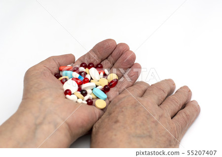 Old hands hold multicolored medical pills. 55207407