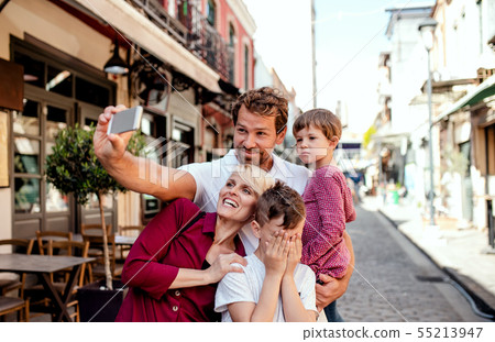 A young family with two small children standing outdoors in town, taking selfie. A young family with two small children standing outdoors in town, taking selfie. 55213947