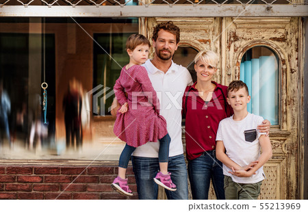 Front view of young family with two small children standing outdoors in town. 55213969
