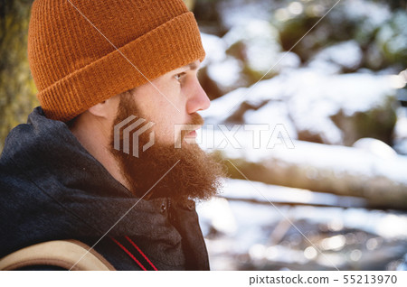 Close-up portrait of a bearded young man in a hat and a backpack in the coniferous forest. The 55213970