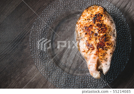 Close-up one grilled cum salmon keta fish steak on a glass transparent plate on a dark wood table 55214085