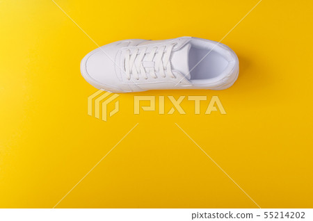 A studio shot of white running shoe on yellow background. Flat lay. A studio shot of white running shoe on yellow background. Flat lay. 55214202