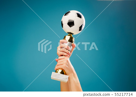 Image of hand holding victory cup with soccer ball on empty blue background 55217714