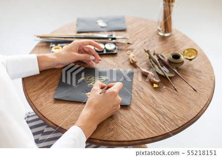 Woman calligrapher is holding a pen with ink and signs a card in handwritten font. Close-up. Soft 55218151