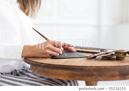 Woman calligrapher is holding a pen with ink and signs a card in handwritten font. Close-up. Soft Woman calligrapher is holding a pen with ink and signs a card in handwritten font. Close-up. Soft 55218153