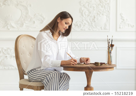 A young beautiful woman sits on a chair in the luxurious interior of a living room and writes a A young beautiful woman sits on a chair in the luxurious interior of a living room and writes a 55218219