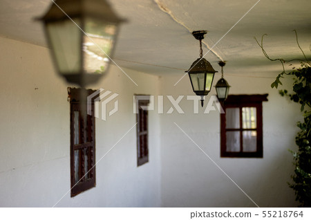 Forged lamps on the open veranda of the whitewashed hut with wooden Windows Forged lamps on the open veranda of the whitewashed hut with wooden Windows 55218764