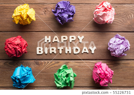Happy birthday phrase and colorful crampled paper ball placed in circle on wooden table 55226731