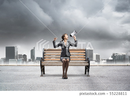 Business woman with megaphone sitting on wooden bench Business woman with megaphone sitting on wooden bench 55228811