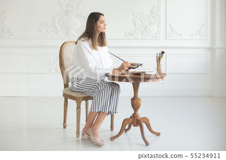 An inspired girl artist holds a palette and a brush in her hands, sits on a chair in the interior of An inspired girl artist holds a palette and a brush in her hands, sits on a chair in the interior of 55234911