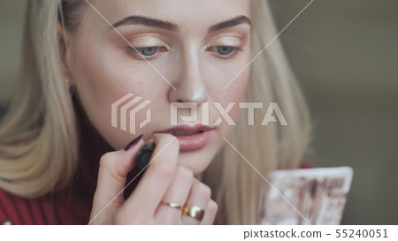 Blond girl paints her lips with lipstick with a dull red color. Blond girl paints her lips with lipstick with a dull red color. 55240051