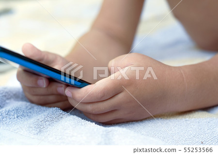 Closeup of kid lying on bath towel with smartphone Closeup of kid lying on bath towel with smartphone 55253566