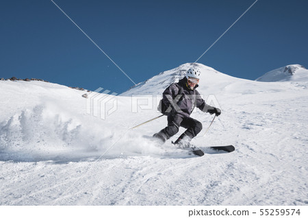 A bearded mature aged male skier in a black ski suit descends along the snowy slope of a ski resort A bearded mature aged male skier in a black ski suit descends along the snowy slope of a ski resort 55259574