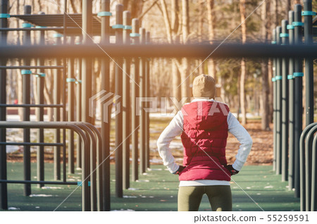 Back view Sports girl in warm clothes on a sunny day does a warm-up on the outdoor sports field in 55259591
