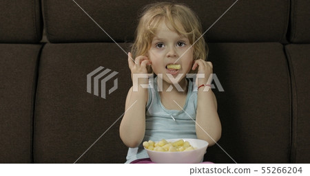 Girl sitting on sofa and eating corn puffs. Child taste puffcorns Girl sitting on sofa and eating corn puffs. Child taste puffcorns 55266204