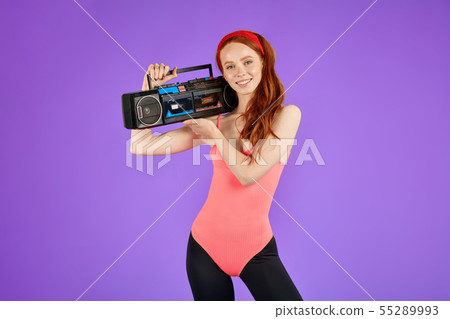 view of athletic girl with red hair and fit body, stands with portable audio player 55289993