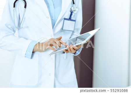 Doctor woman using tablet in clinic office. Unknown female physician at work while standing straight 55291086