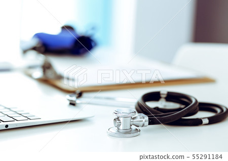 Closeup of stethoscope. Female doctor fills up medical form while sitting at the desk in hospital 55291184