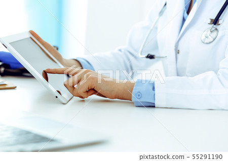Doctor working table. Woman physician using tablet computer while sitting in hospital office close Doctor working table. Woman physician using tablet computer while sitting in hospital office close 55291190