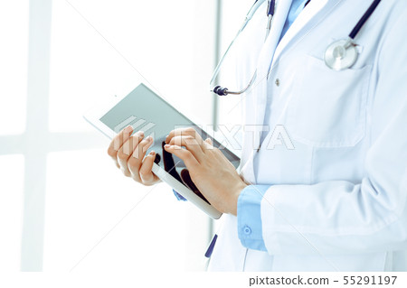 Woman doctor using tablet computer while standing straight in hospital closeup. Healthcare Woman doctor using tablet computer while standing straight in hospital closeup. Healthcare 55291197