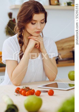 Young woman looking for a new recipe for cooking in a kitchen. Housewife is making online shopping Young woman looking for a new recipe for cooking in a kitchen. Housewife is making online shopping 55291353
