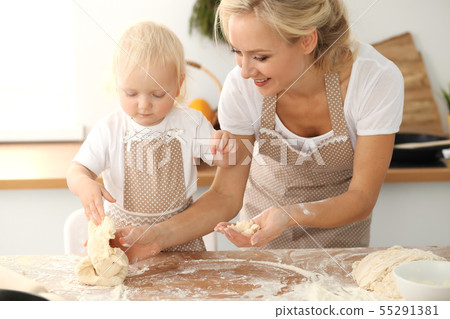 Little girl and her blonde mom in beige aprons playing and laughing while kneading the dough in Little girl and her blonde mom in beige aprons playing and laughing while kneading the dough in 55291381