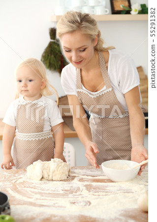 Little girl and her blonde mom in beige aprons playing and laughing while kneading the dough in Little girl and her blonde mom in beige aprons playing and laughing while kneading the dough in 55291382
