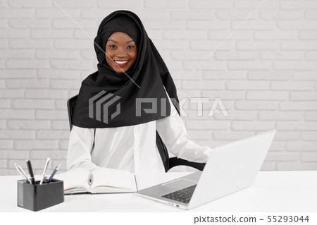 Muslim woman sitting at table with white laptop in office. 55293044