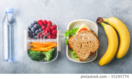 School lunch box with sandwich vegetables water almonds and fruits on grey table healthy School lunch box with sandwich vegetables water almonds and fruits on grey table healthy 55295774