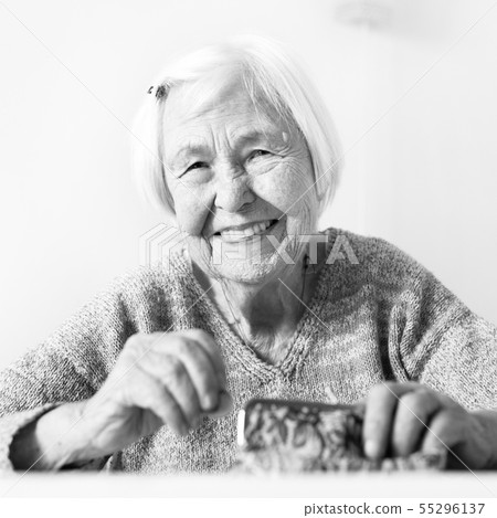 Cheerful elderly 96 years old woman sitting at table at home happy with her pension savings in her Cheerful elderly 96 years old woman sitting at table at home happy with her pension savings in her 55296137